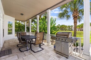 Eine überdachte Terrasse mit Grill, Esstisch und Stühlen.