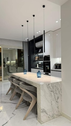A modern kitchen with a marble island, pendant lights, and built-in appliances.