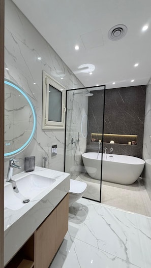 A modern bathroom with a large mirror, two sinks, a bathtub, and a shower enclosure.