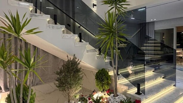 Un interior modern amb una escala central, plantes d'interior i un terra de marbre.