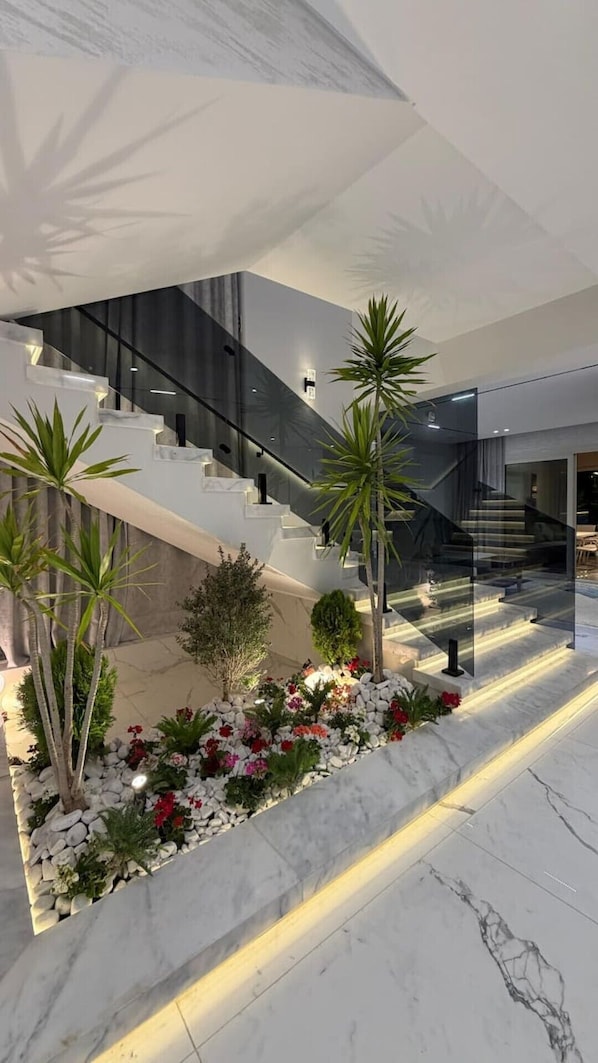 A modern interior with a central staircase, indoor plants, and a marble floor.