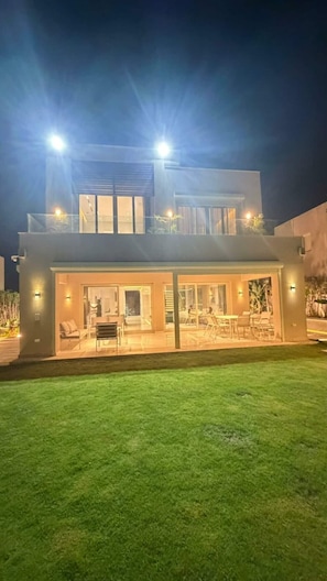 A modern two-story building with a glass facade, outdoor seating area, and illuminated windows.
