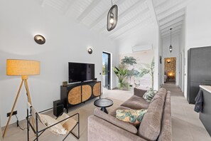 A modern living room with a flat-screen TV, a sofa, a lamp, and a dining area with a table and chairs.
