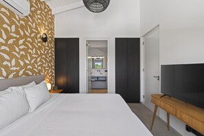 A bedroom with a bed, a TV, a wardrobe, and a bathroom visible through an open door. - Curadise Penthouse - luxury poolside apartment in Jan Thiel (Jan Thiel)