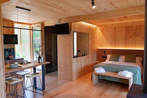 Een houten interieur met een bed, een bureau met krukken, een televisie en een groot raam.