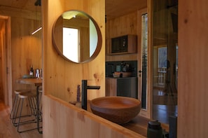 A wooden interior with a round mirror, a wooden sink, and a bar stool.