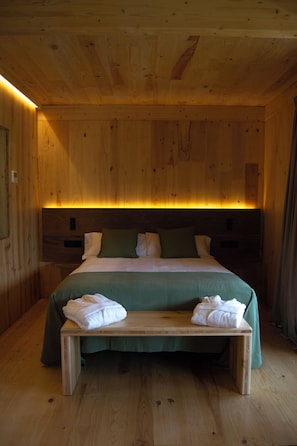 Een kamer met houten lambrisering, een bed, een bankje en nachtkastjes.