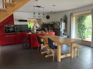 A modern kitchen with red cabinets, a wooden dining table, and a large window. - Bioclimatic villa with natural garden at the end of a cul-de-sac, quiet neighborhood. (Montauroux)