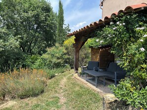 A covered outdoor seating area with a pergola, surrounded by lush greenery and a variety of plants. - Bioclimatic villa with natural garden at the end of a cul-de-sac, quiet neighborhood. (Montauroux)