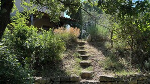 Uma escadaria de pedra serpenteia por uma colina, rodeada por vegetação e com um edifício ao fundo.