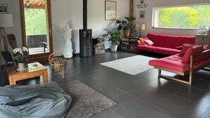Uma sala de estar moderna com um sofá vermelho, uma lareira a lenha preta, um tapete branco e uma grande janela com vista para o verde.