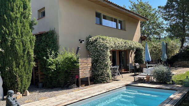 Uma piscina com deck de madeira, um alpendre coberto com mobiliário externo e um edifício com telhado telhado.