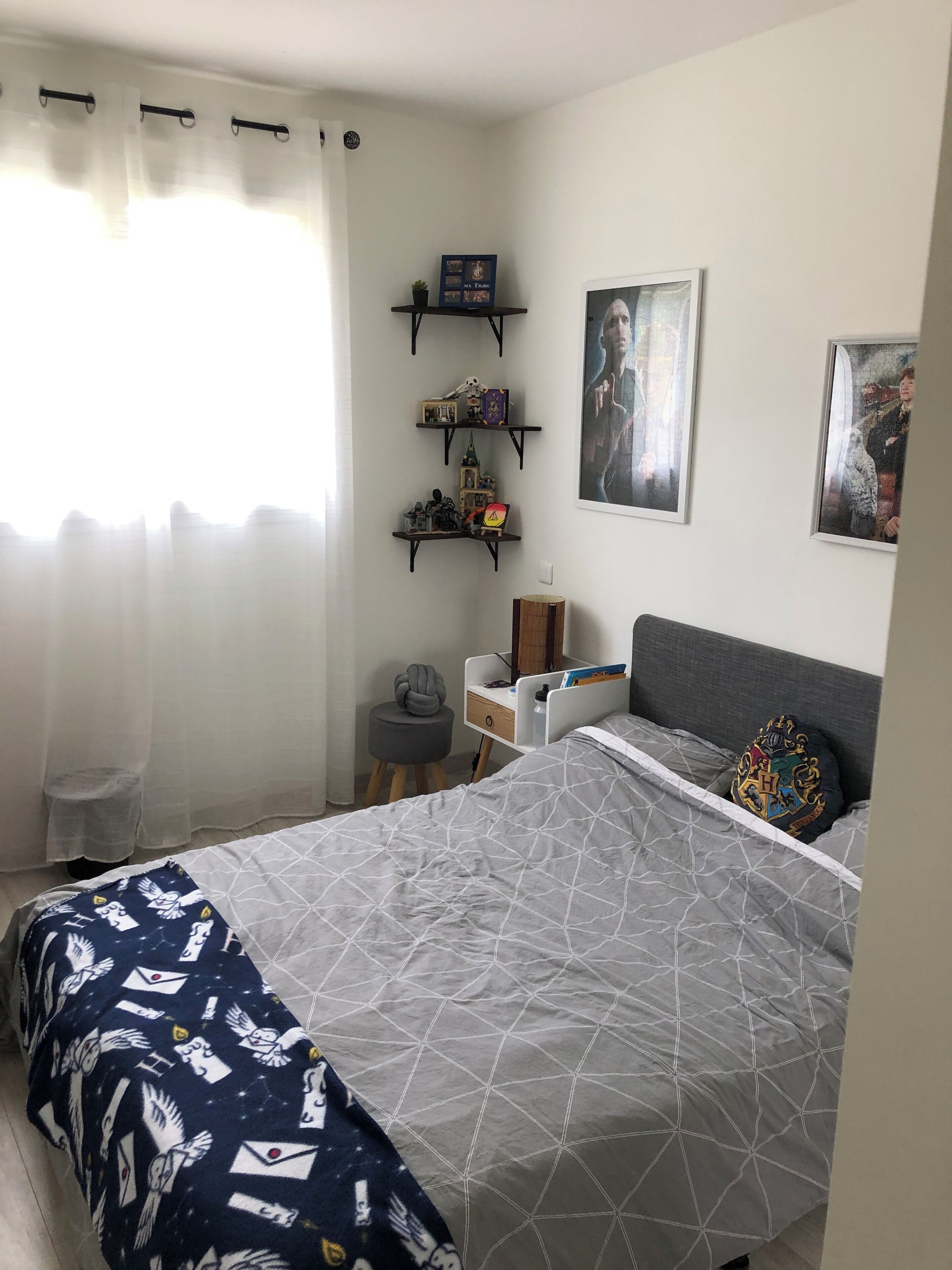 Ett sovrum med en säng, ett skrivbord, en stol och hyllor med diverse föremål.