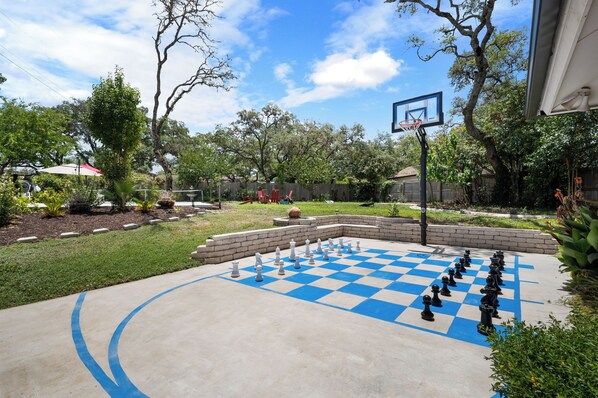 A checkered outdoor game area with a basketball hoop and surrounding greenery.