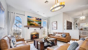 A living room with leather sofas, a fireplace, and a large painting of a beach scene. - Luxury Pool, Hot Tub, Pickleball, Family Resort Getaway! (San Antonio)