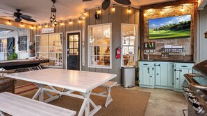A kitchen with a large TV, wooden cabinets, and a dining area with a table and benches. - Luxury Pool, Hot Tub, Pickleball, Family Resort Getaway! (San Antonio)