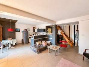En kompakt opholdsstue med tekøkken, spiseplads, sofa, sofabord og trappe.