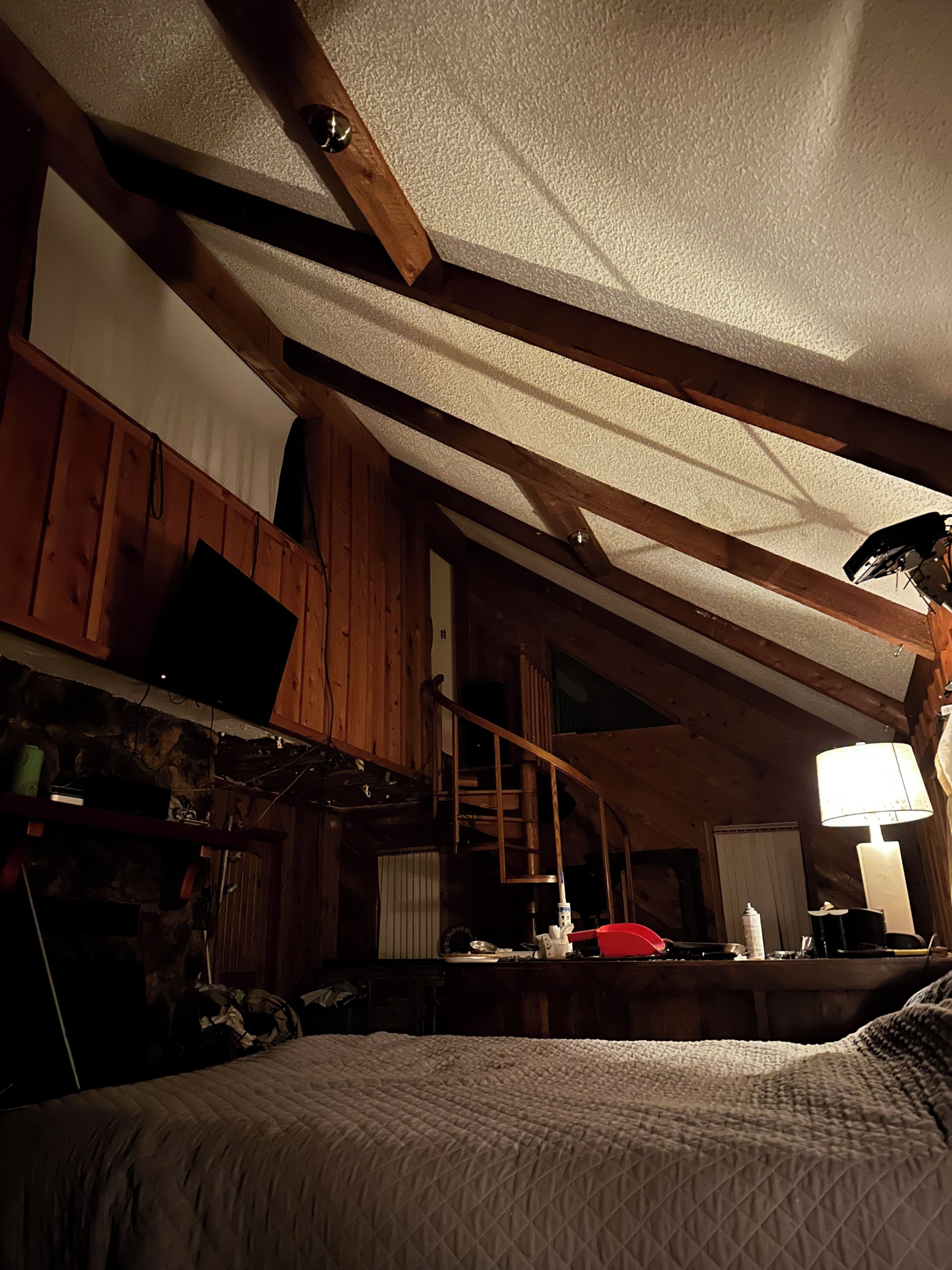 Una habitación con techo inclinado, vigas de madera, una cama, un escritorio y una silla.