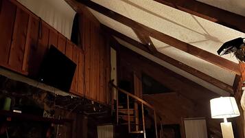 Una habitación con techo inclinado, vigas de madera, una cama, un escritorio y una silla.