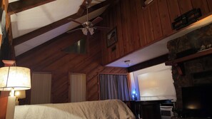 A cozy room with a bed, a ceiling fan, a fireplace, and a television.
