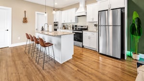 A modern kitchen with white cabinets, a stainless steel refrigerator, and a bar area with stools. - Music City House, Sleeps 12 and Very close to Broadway, DT (Nashville)