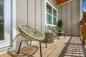 Eine Holzterrasse mit zwei Korbstühlen, einem kleinen runden Tisch und einem Blumentopf.