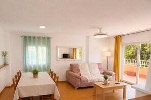 Ein Wohnzimmer mit Esstisch, Sofa und einem großen Fenster mit Vorhängen.