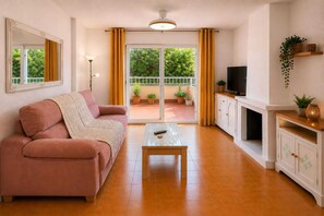 Ein Wohnzimmer mit einer Couch, einem Couchtisch, einem Fernseher und einem Balkon mit Topfpflanzen.