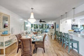 A modern kitchen with white cabinets, a dining area with wicker chairs, and a large window. - Your tropical oasis awaits your arrival in siesta key. (Siesta Key)