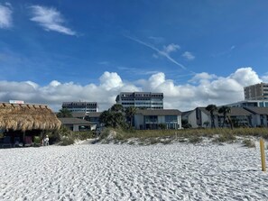 A beach with buildings, including a thatched-roof structure and modern buildings with large windows. - Your tropical oasis awaits your arrival in siesta key. (Siesta Key)