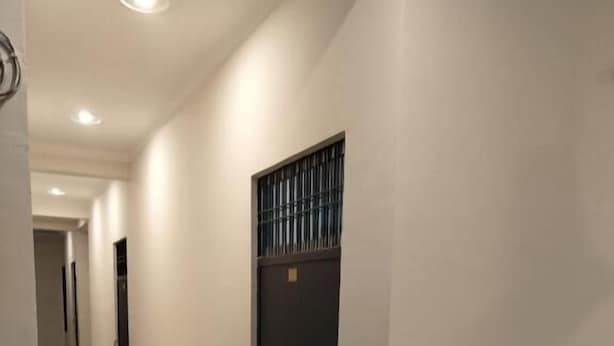 Um corredor com porta escura, paredes brancas e chão de azulejos.