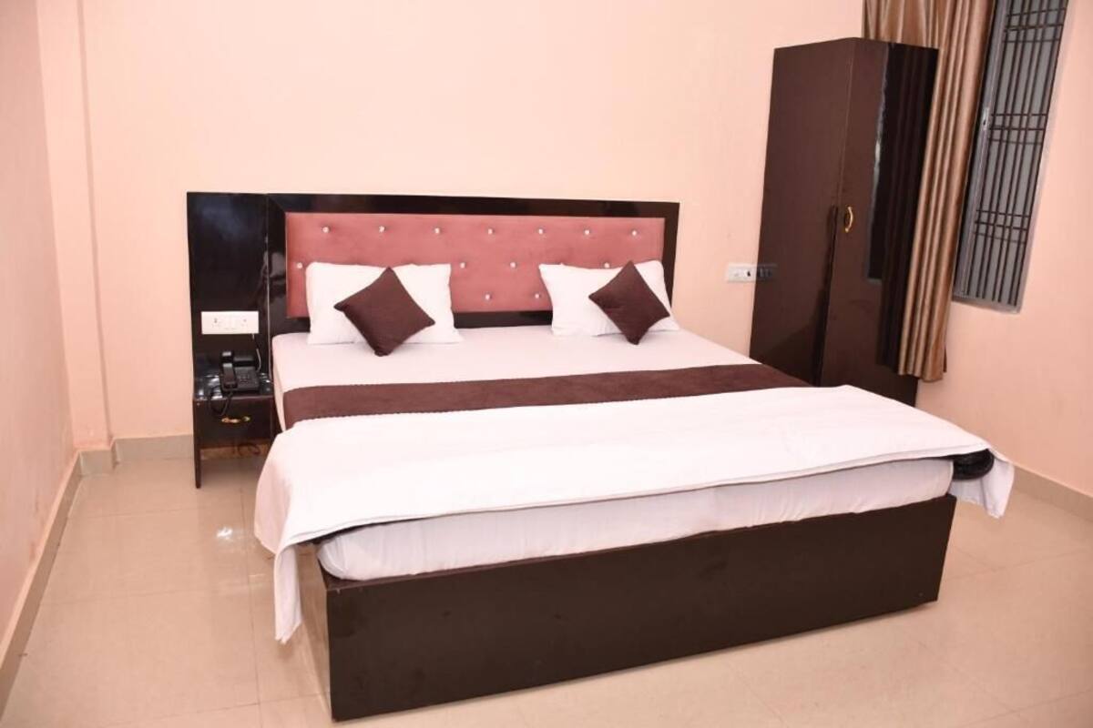 Quarto com cama grande, mesa de cabeceira, guarda-roupa e janela com grades.