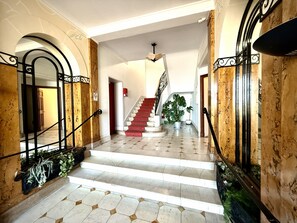 Una imponente escalera con alfombra roja, paredes de mármol y barandilla de metal.