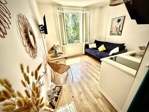 Ein kompakter Wohnbereich mit Sofa, Esstisch, Küchenzeile und großem Fenster.