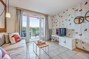 A modern living room with a sofa, a coffee table, a TV on a stand, and a balcony with curtains. - Couples Retreat in Houlgate With Spa (Houlgate)