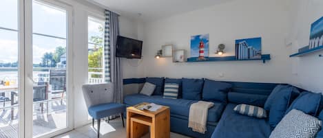 A modern living room with a blue sofa, a wooden coffee table, and a TV mounted on the wall.