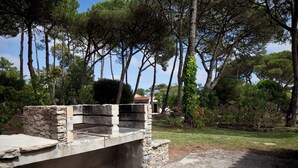 A stone barbecue area with a view of tall trees and a garden.