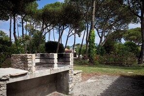 A stone barbecue area with a view of tall trees and a garden.