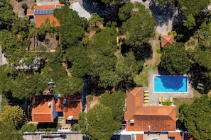 An aerial view of a residential area with multiple houses, a swimming pool, and surrounding greenery.