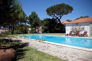 Une piscine avec des chaises longues, un chemin en pierre et un bâtiment doté d’un toit en tuiles.