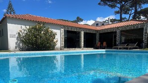 A swimming pool with clear blue water, a stone building with a tiled roof, and a few lounge chairs.