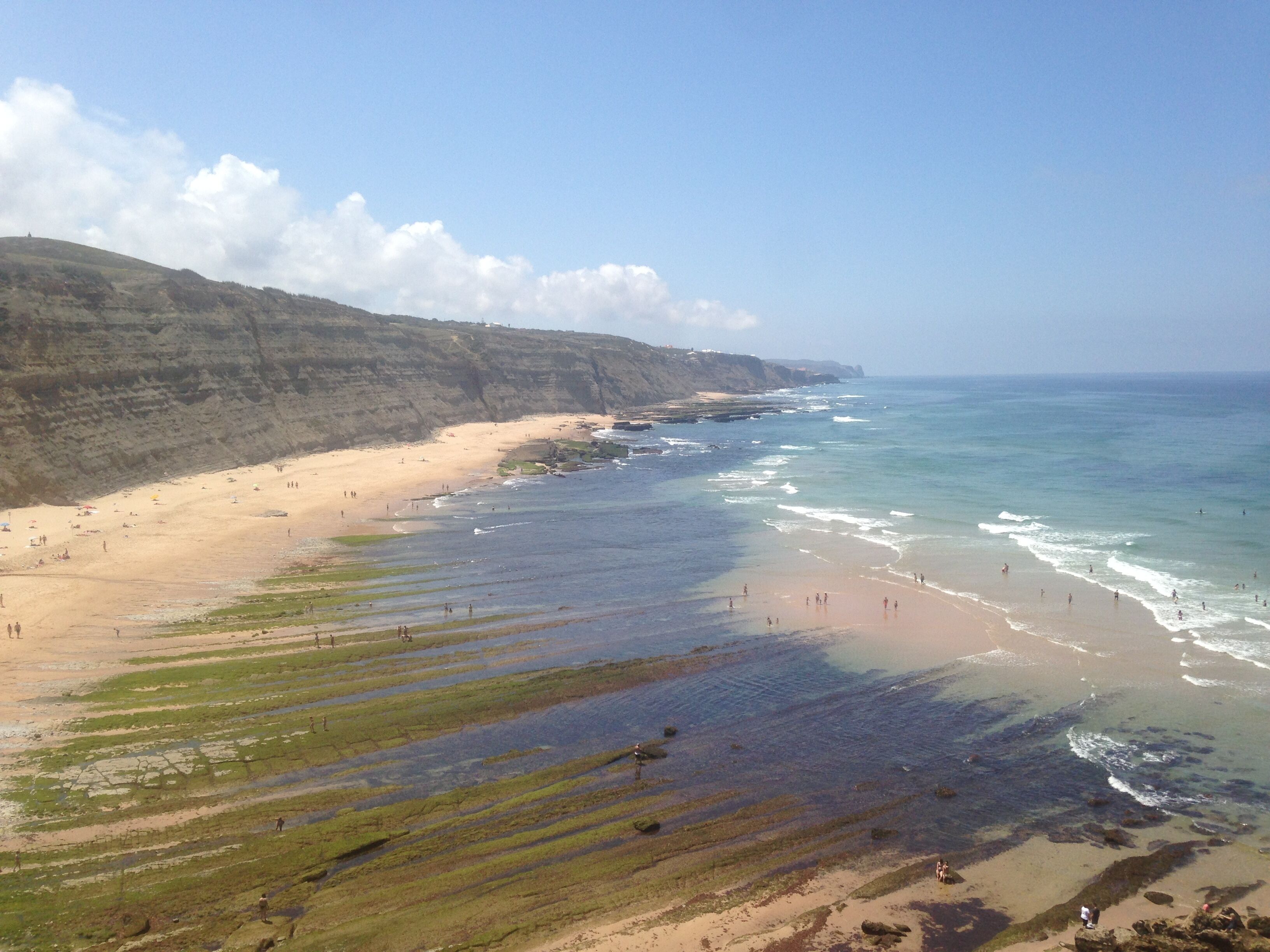 A coastal beach with a sandy shore, rocky outcrops, and clear blue water.