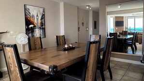 A dining area with a wooden table and chairs, a ceiling fan, and a large mirror reflecting the room. - Sky Beachfront Escape, 180 degree ocean view, 15th floor (Cape Town)