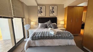 A bedroom with a bed, bedside tables, a nightstand, a wardrobe, and two wall-mounted zebra paintings. - Sky Beachfront Escape, 180 degree ocean view, 15th floor (Cape Town)