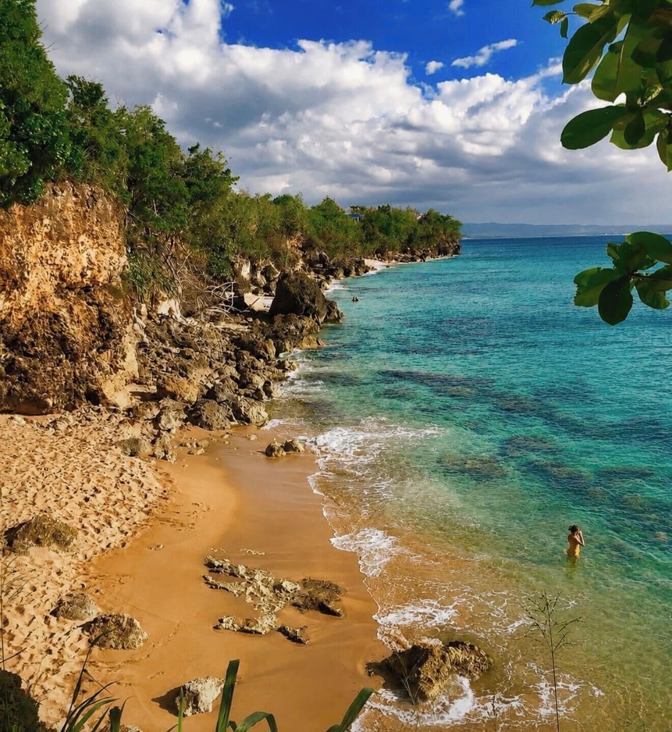 A beach with clear turquoise water, sandy shore, and rocky cliffs.
