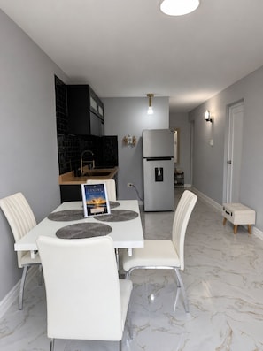 A modern kitchen with a refrigerator, a dining table with chairs, and a small bench. - Apartment  in Aguadilla with beach access apt B (Aguadilla)