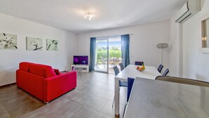A modern living room with a red sofa, a dining table, and a TV. - Corsican Flat With Pergola (Lecci)