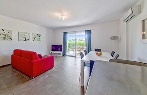 A modern living room with a red sofa, a dining table, and a TV. - Corsican Flat With Pergola (Lecci)