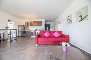 A modern living room with a red sofa, a dining area with bar stools, a kitchen in the background, and a potted plant on a table. - Corsican Flat With Pergola (Lecci)