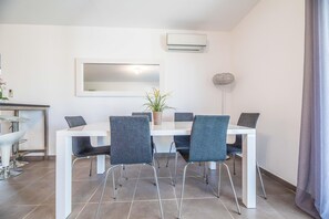 A modern dining area with a white table, four grey chairs, a potted plant, and an air conditioning unit on the wall. - Corsican Flat With Pergola (Lecci)